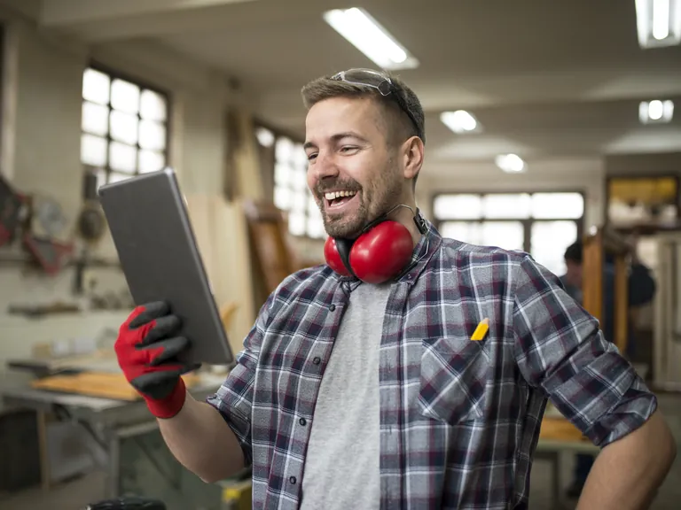 A cheerful woodworker looking at a tablet in his workshop
