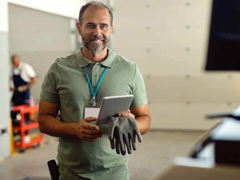 A smiling workshop foreman holding a tablet and work gloves