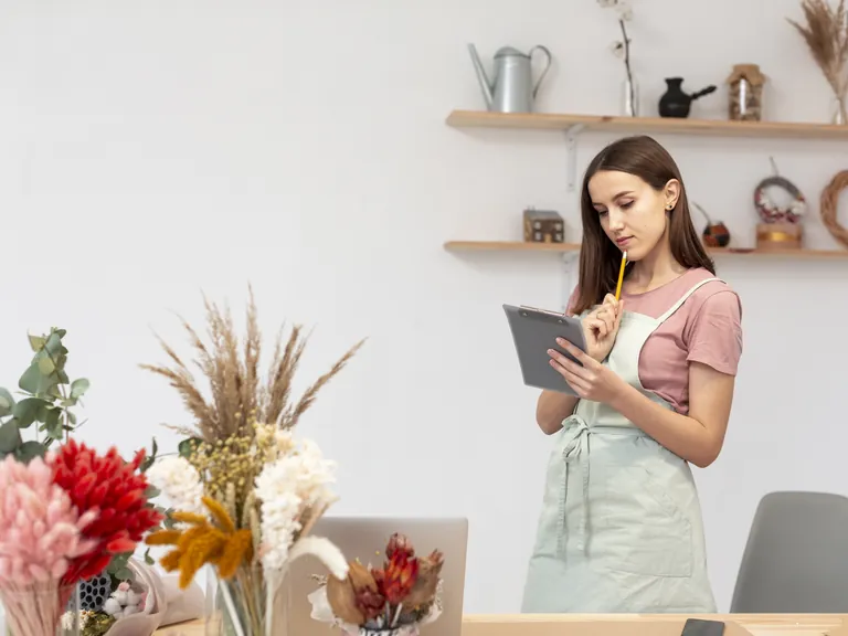 A smiling woman in an apron using a tablet in her own shop