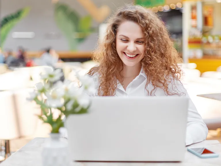 A smiling woman with curly hair working on a laptop at a table with flowers