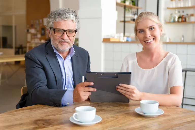 Two people talking over coffee while looking at documents on a tablet