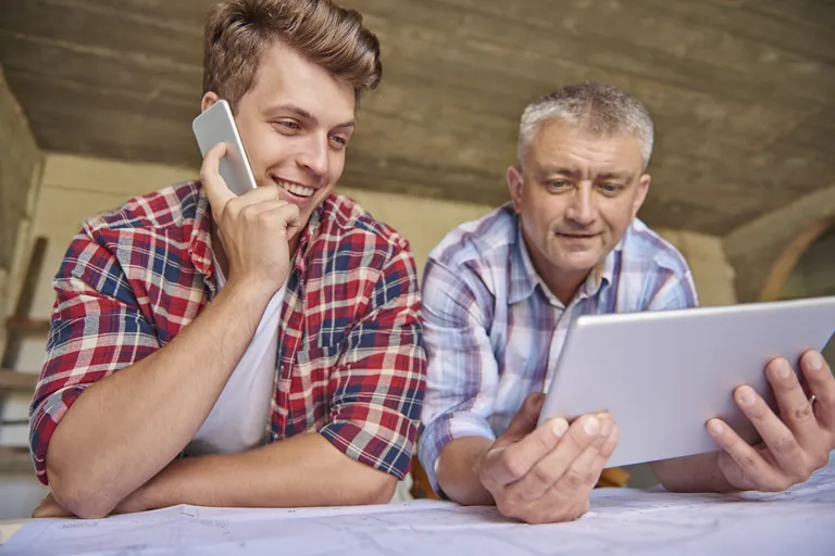 Two tradesmen looking at a tablet together while one takes a phone call