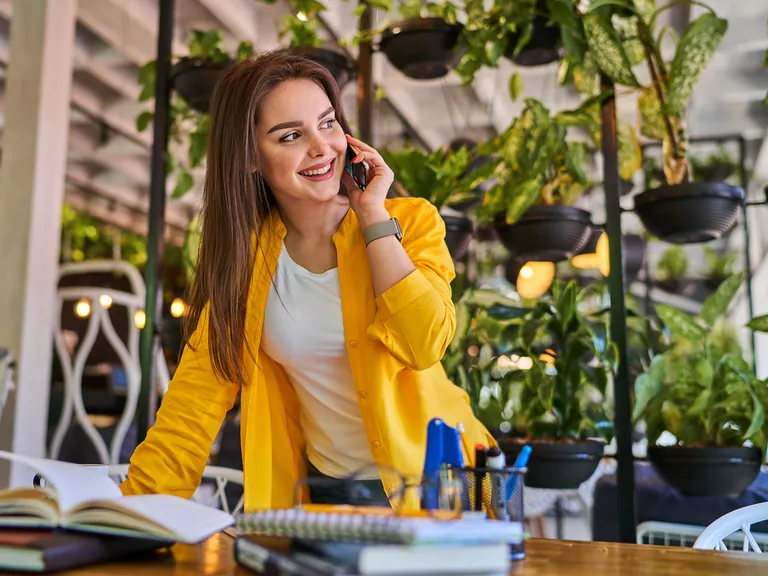 A smiling woman talking on her mobile phone at a desk surrounded by plants