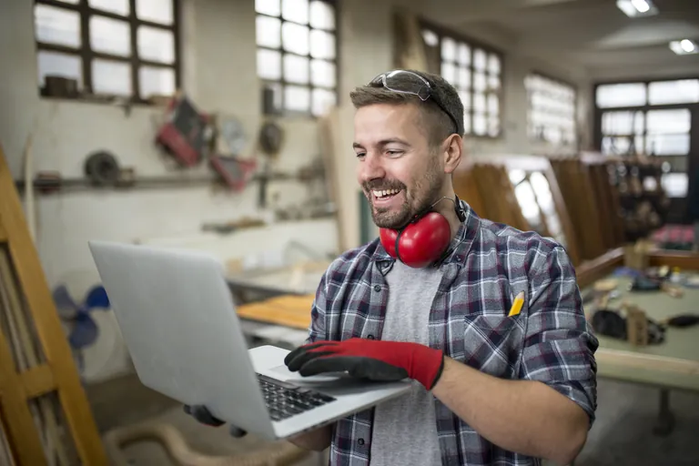 A smiling carpenter working on a laptop in his workshop