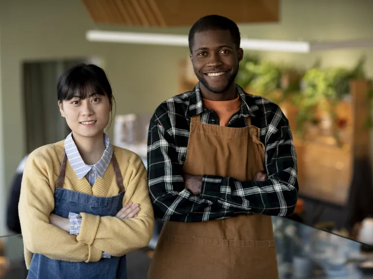 Two smiling small business owners in aprons standing with their arms crossed