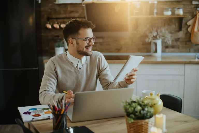 A smiling man working at a laptop and tablet at home
