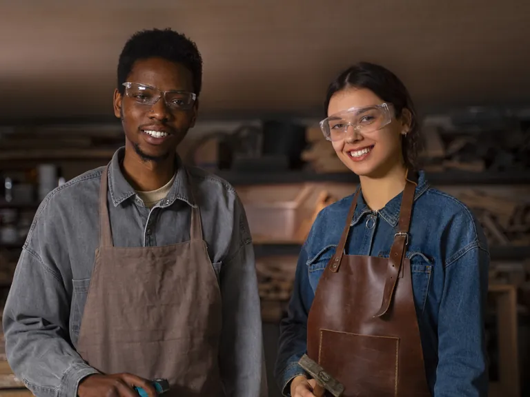 Two smiling craftspeople in aprons in their workshop