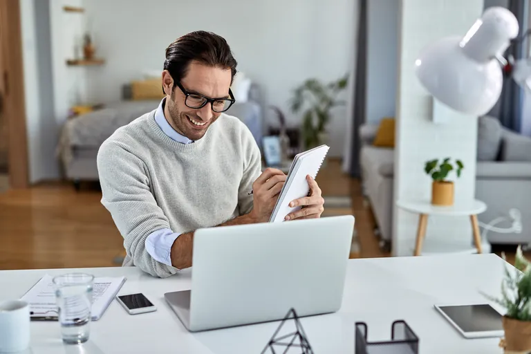 A smiling man using a tablet beside his laptop at home